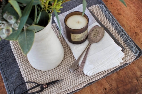 Top down view of wooden table with vase of eucalyptus, old fashioned scissors, candle and spoons - Australian Stock Image