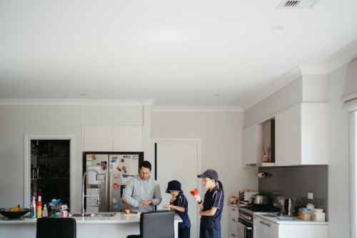 Middle-aged dad cutting fruit on the kitchen counter with his kids getting school snacks ready - Australian Stock Image