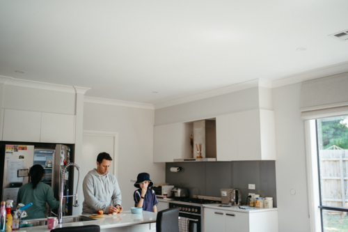 Middle-aged guy cutting fruit on the kitchen counter with the kids for school lunch - Australian Stock Image