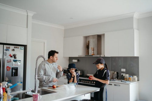 Middle-aged guy cutting fruits on the kitchen counter with the kids. - Australian Stock Image