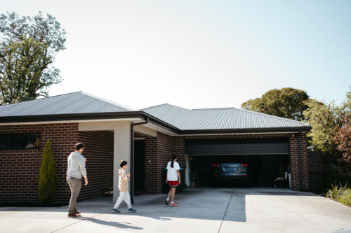 Middle-aged man with his kids walking towards the car parked in the garage. - Australian Stock Image