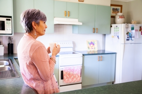 Middle aged woman drinking a cup of tea in her kitchen - Australian Stock Image