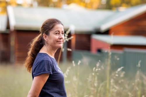 middle-aged woman outside with rustic house and wild oats in background - Australian Stock Image