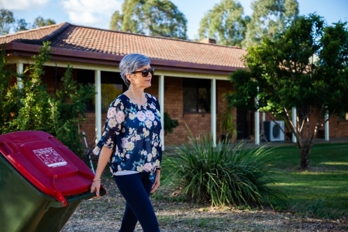 Middle aged woman taking rubbish bin out for collection - Australian Stock Image