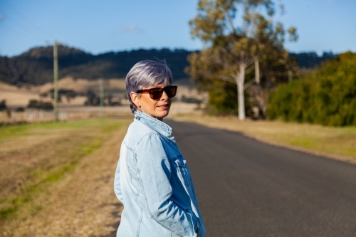 Middle aged woman walking down a rural road for exercise - Australian Stock Image