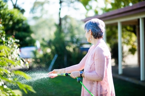 Middle aged woman watering her garden beside her house - Australian Stock Image