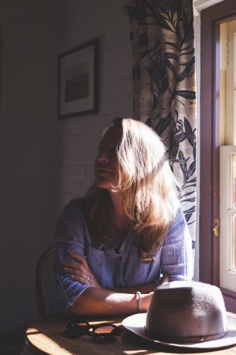 Middle-aged woman with brown hair sitting near the window. - Australian Stock Image