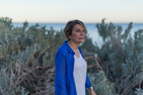 Middle eastern woman walking on shoreline at dusk - Australian Stock Image