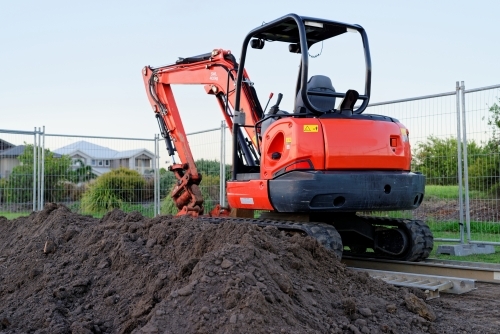 Mini digger standing idle at a construction site - red excavator - Australian Stock Image