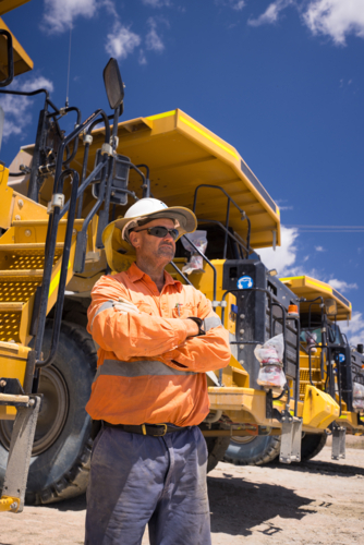 Mining operator man with arms crossed standing next to a huge dump truck on mine site - Australian Stock Image