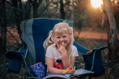 Mischievous girl smiling while drawing at camp - Australian Stock Image