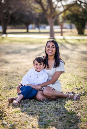 Mixed race aboriginal and caucasian boy sitting on grass with aboriginal mother