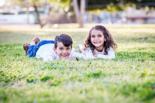 Mixed race aboriginal and caucasian twin brother and sister lying on grass smiling