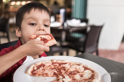 Mixed race boy eating pizza at a suburban Italian restaurant - Australian Stock Image