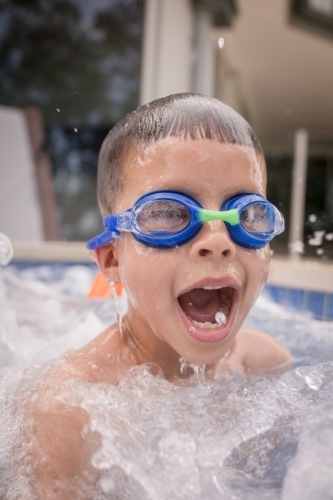 Mixed race boy swims and plays in a backyard pool - Australian Stock Image