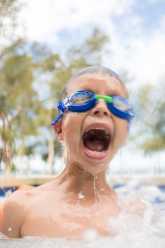 Mixed race boy swims and plays in a backyard pool - Australian Stock Image