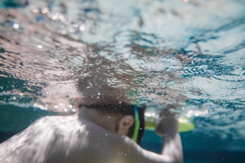 Mixed race boy swims and plays in a backyard pool - Australian Stock Image