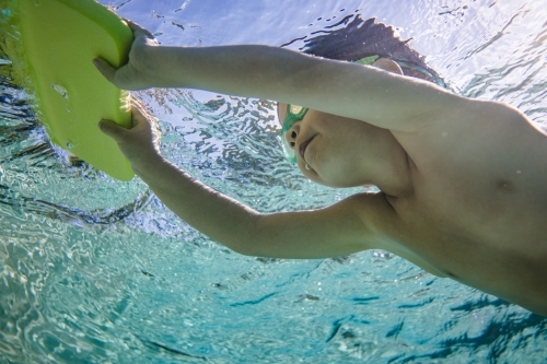 Mixed race boy swims and plays in a backyard pool - Australian Stock Image