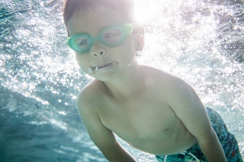 Mixed race boy swims and plays in a backyard pool - Australian Stock Image