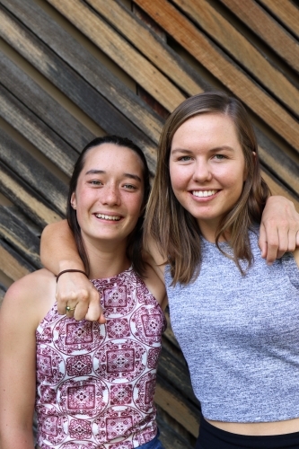 Mixed race sisters smiling in front of textured wooden paneling - Australian Stock Image