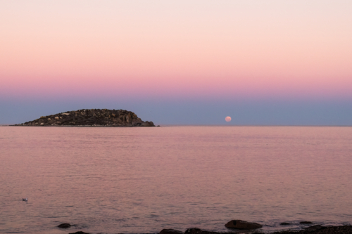 Moon going down over water with rocky island in foreground, Victor Harbor, South Australia - Australian Stock Image