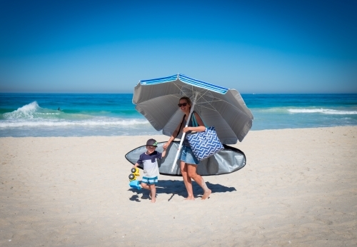 Mother and child walking on beach holding large beach umbrella - Australian Stock Image