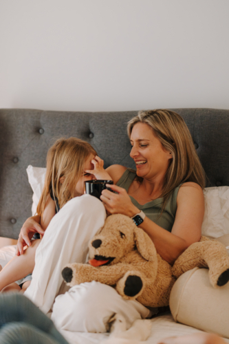 Mother and daughter cuddling on the bed with a stuffed animal. - Australian Stock Image