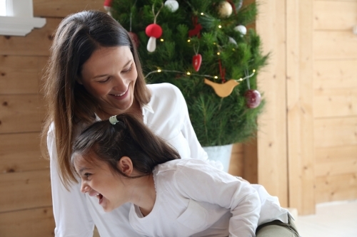 Mother and daughter laughing together in front of Christmas tree - Australian Stock Image