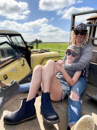 Mother and daughter sitting on old farm equipment embracing - Australian Stock Image