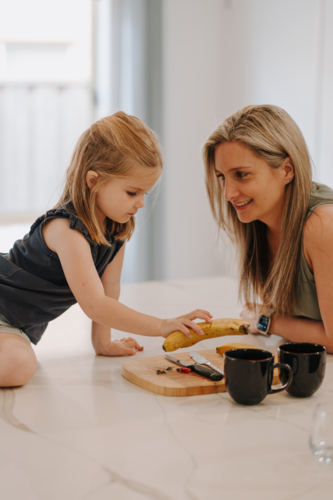 Mother and daughter sitting together with chopping board and mugs - Australian Stock Image