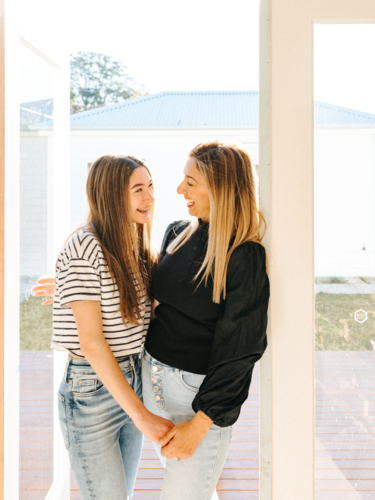 Mother and daughter standing in the doorway smiling while looking at each other. - Australian Stock Image