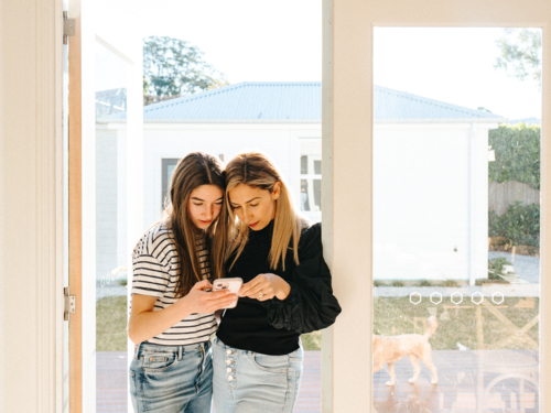 Mother and daughter standing in the doorway while looking on the phone. - Australian Stock Image