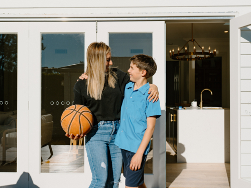 Mother and son looking at each other outside the house holding a basketball. - Australian Stock Image