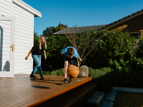 Mother and son playing basketball on the wooden deck. - Australian Stock Image