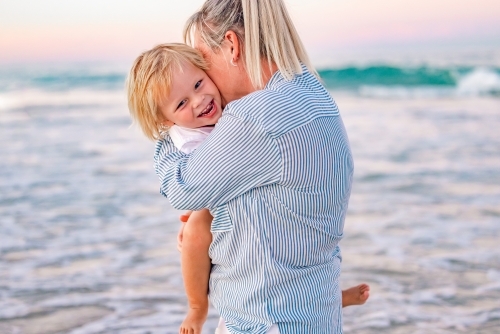 Mother and toddler son embracing on the beach with pink sunset sky - Australian Stock Image
