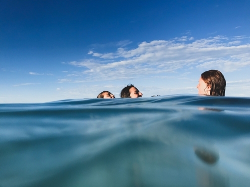 Mother and two boys playing together in ocean on calm day - Australian Stock Image