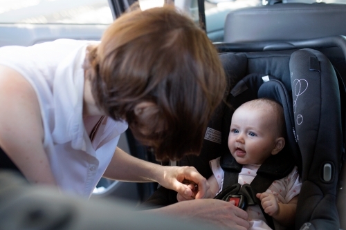 Mother buckling in her baby sitting in rear-facing car seat - Australian Stock Image