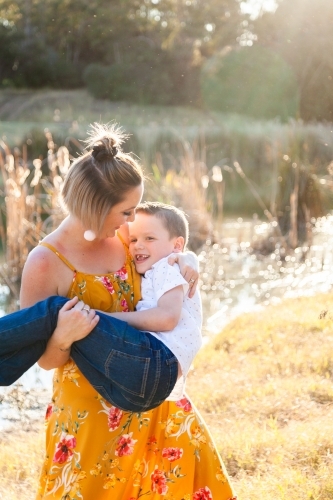 Mother carrying son, spinning outside in the sunlight - Australian Stock Image