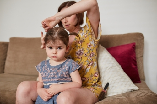 Mother doing toddler girl's hair in loungeroom - Australian Stock Image