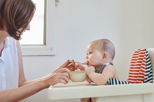 Mother feeding baby girl in high chair - Australian Stock Image