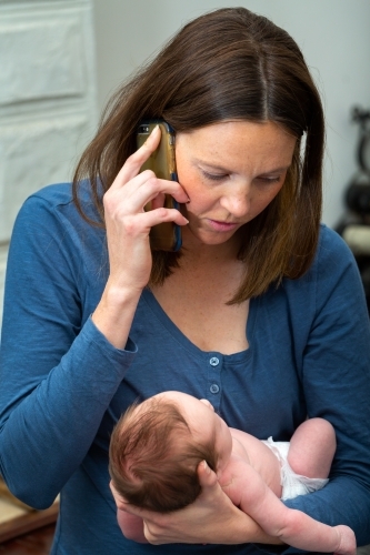 Mother holding newborn baby and talking on phone - Australian Stock Image