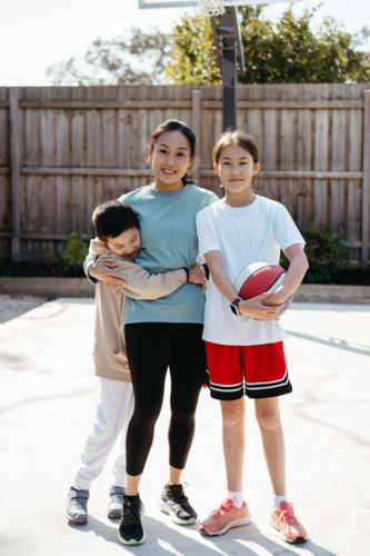 Mother hugs her two young children outside in their backyard. - Australian Stock Image