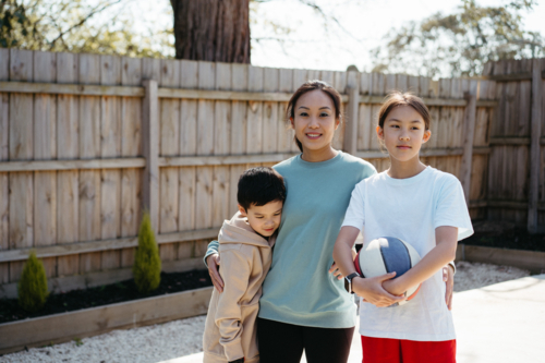 Mother hugs her two young children outside in their backyard. - Australian Stock Image