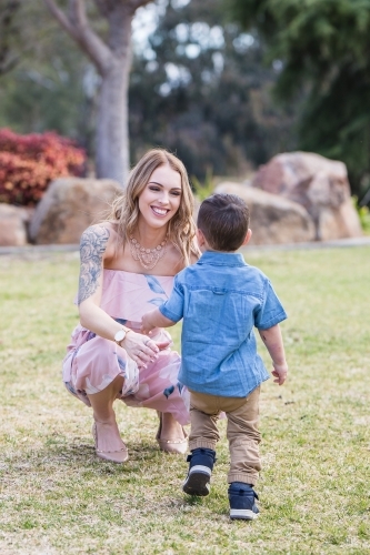 Mother kneeling down with arms outstretched to son running towards her - Australian Stock Image