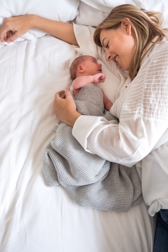 Mother lies beside newborn and smiles. - Australian Stock Image