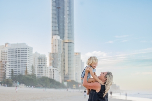 Mother lifting son in the air on Surfers Paradise beach with skyscrapers in background - Australian Stock Image