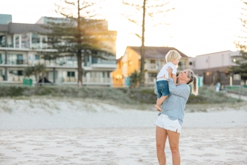 Mother lifting toddler son, playing on Gold Coast beach - Australian Stock Image