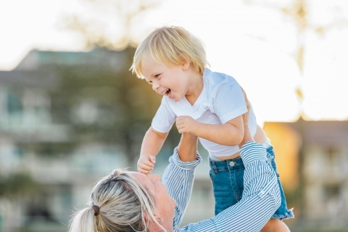 Mother lifting toddler son, playing on Gold Coast beach - Australian Stock Image