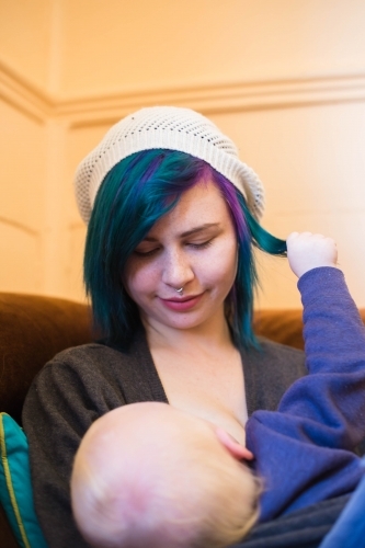 Mother looking down at child breastfeeding while child plays with hair - Australian Stock Image