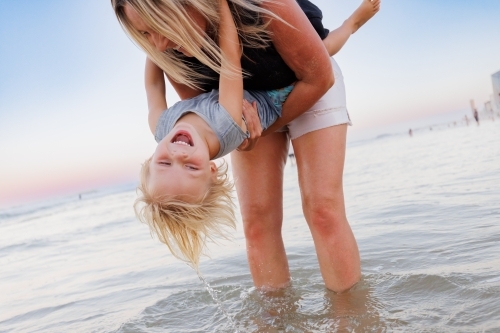 Mother lowering son into water on the beach at the Gold Coast - Australian Stock Image